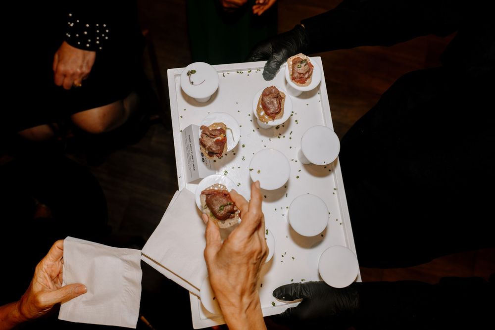 Overhead view of hands reaching for gourmet appetizers on a white tray at an elegant catered event.