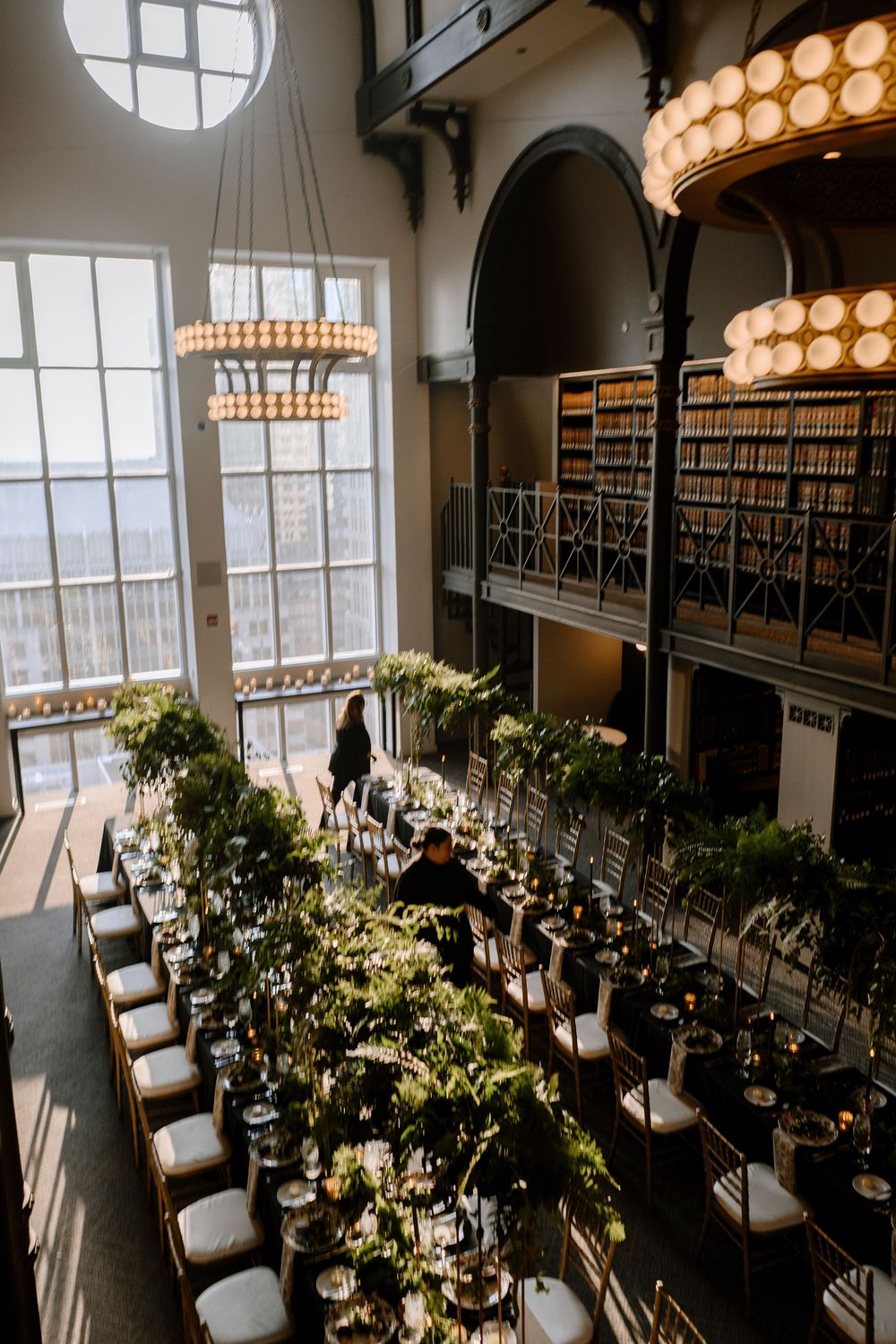 Aerial view of an elegant wedding reception in a historic library venue with lush greenery table runners and chandelier lighting.