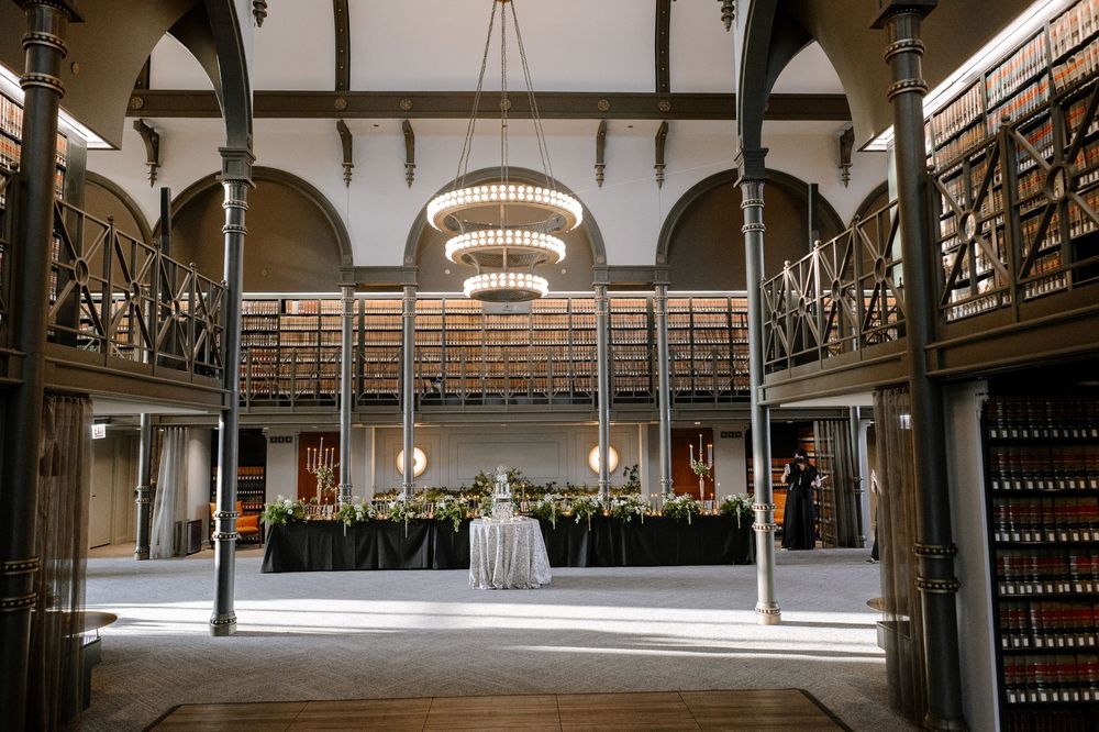 Elegant library event space with chandeliers, bookshelves, and a floral centerpiece table under grand arched ceilings.