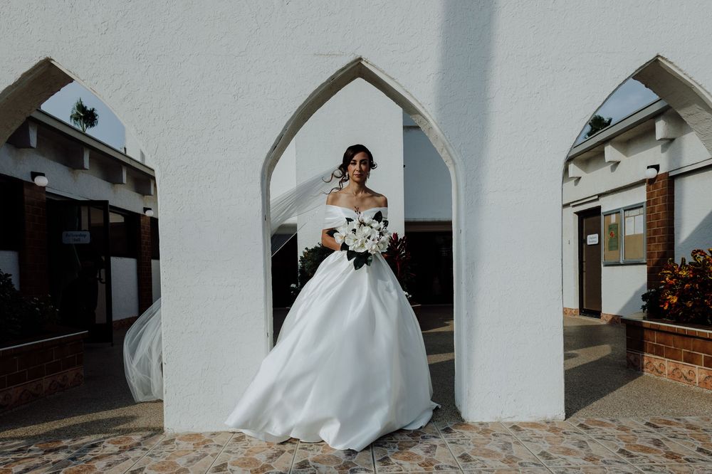 Bride in white ball gown walking through arched doorway of white church.