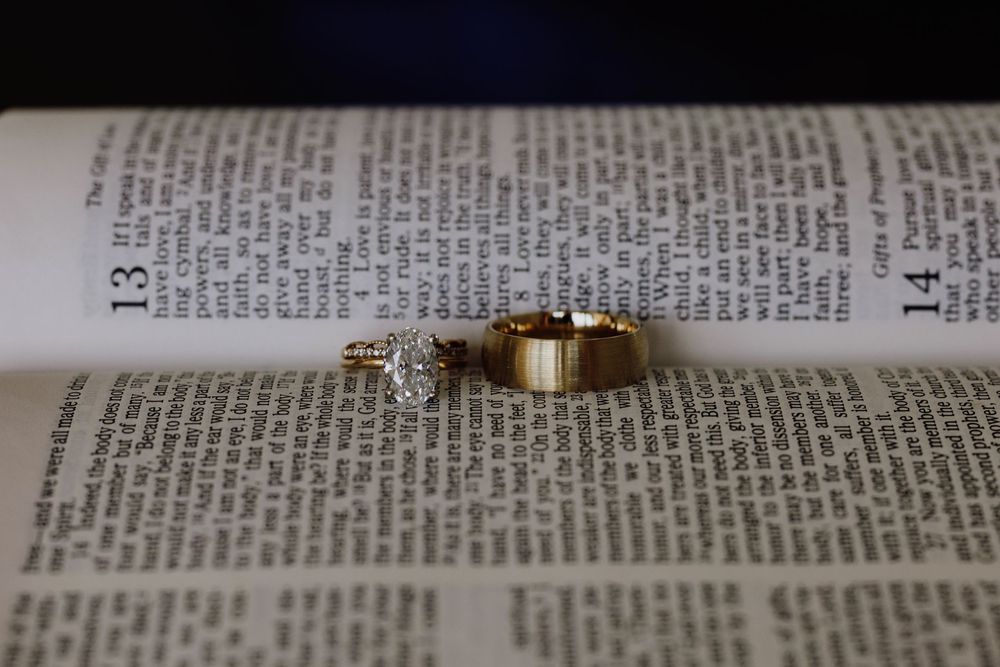 Gold wedding rings and diamond engagement ring displayed on an open Bible page.