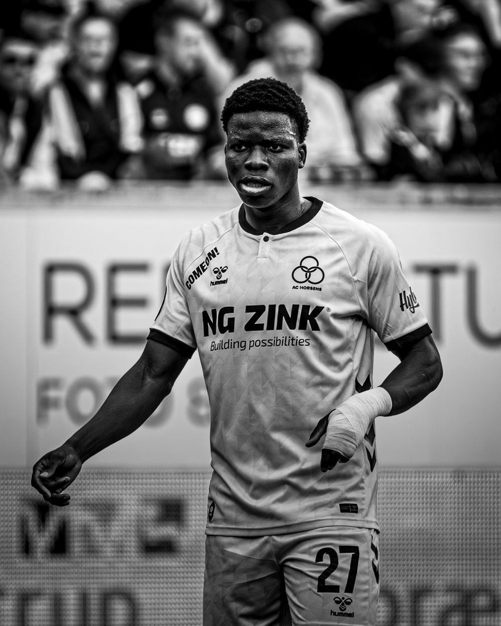 Black and white photo of a young footballer wearing number 27 jersey with NG Zink sponsor during a match.