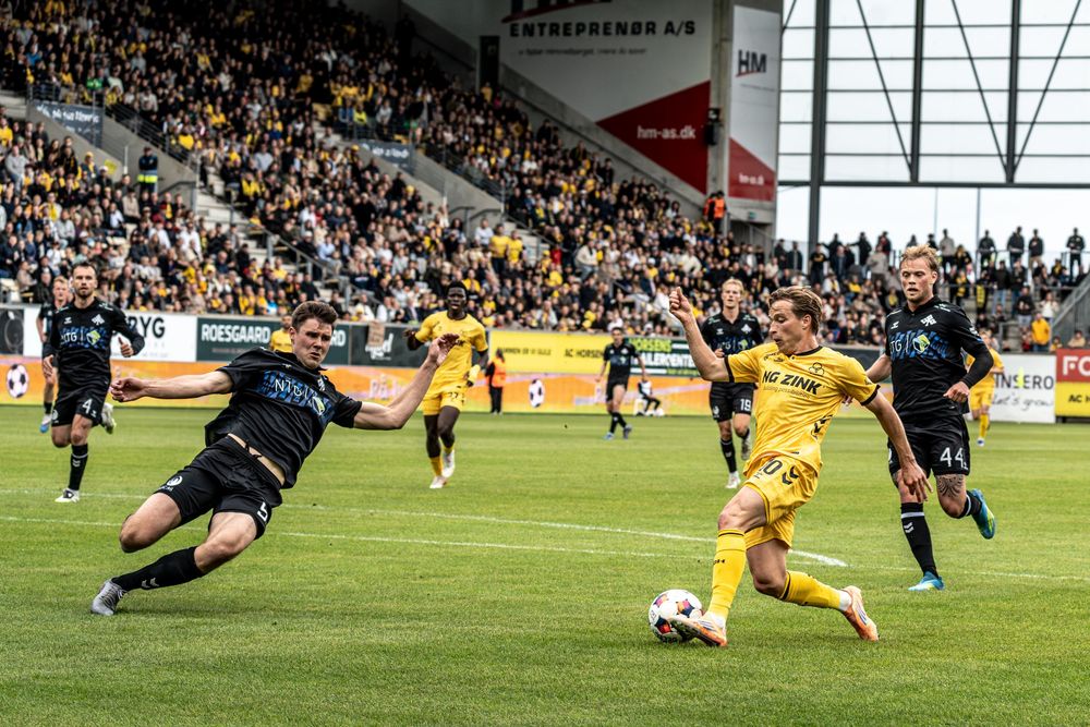 Soccer players compete for the ball during a professional match in a packed stadium with yellow and black team colors.