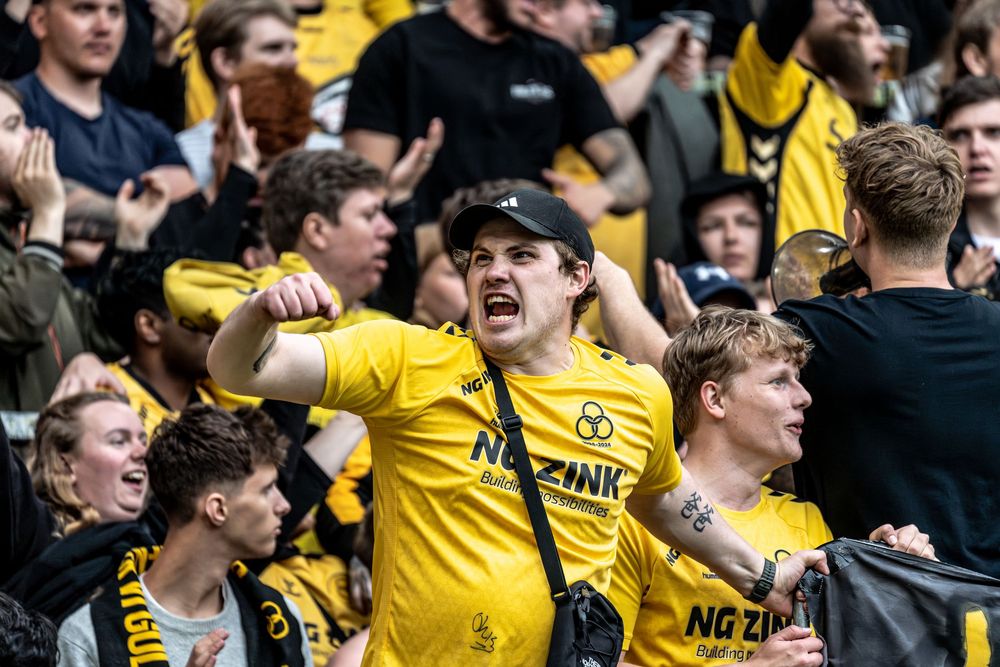 Passionate AC Horsens football fan in yellow NG Zink jersey cheering loudly in stadium stands.