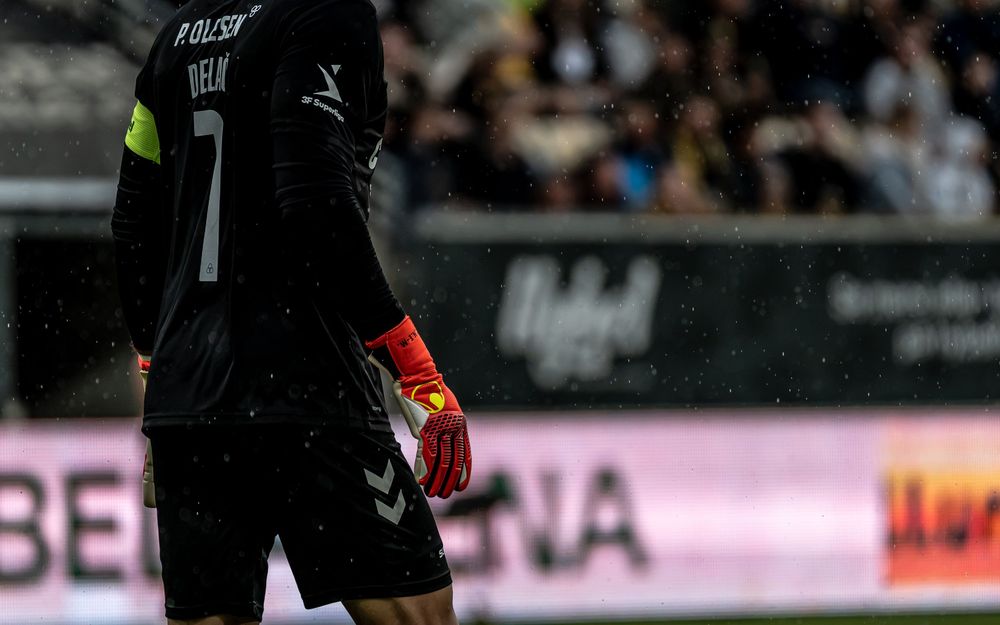 Goalkeeper in black uniform with red gloves and number 7 jersey stands on soccer field during a rainy match.