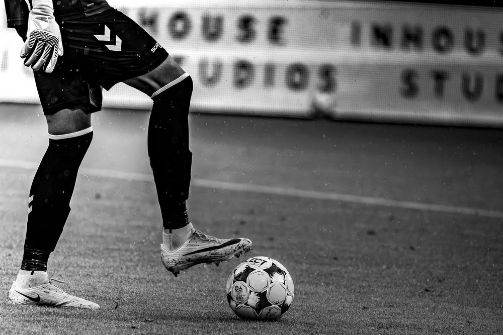 Black and white photo of a soccer player about to kick a ball on a field with an Inhouse Studios advertisement banner.