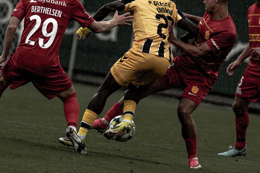 Soccer players in red and yellow jerseys compete for the ball during an intense match on a rainy day.