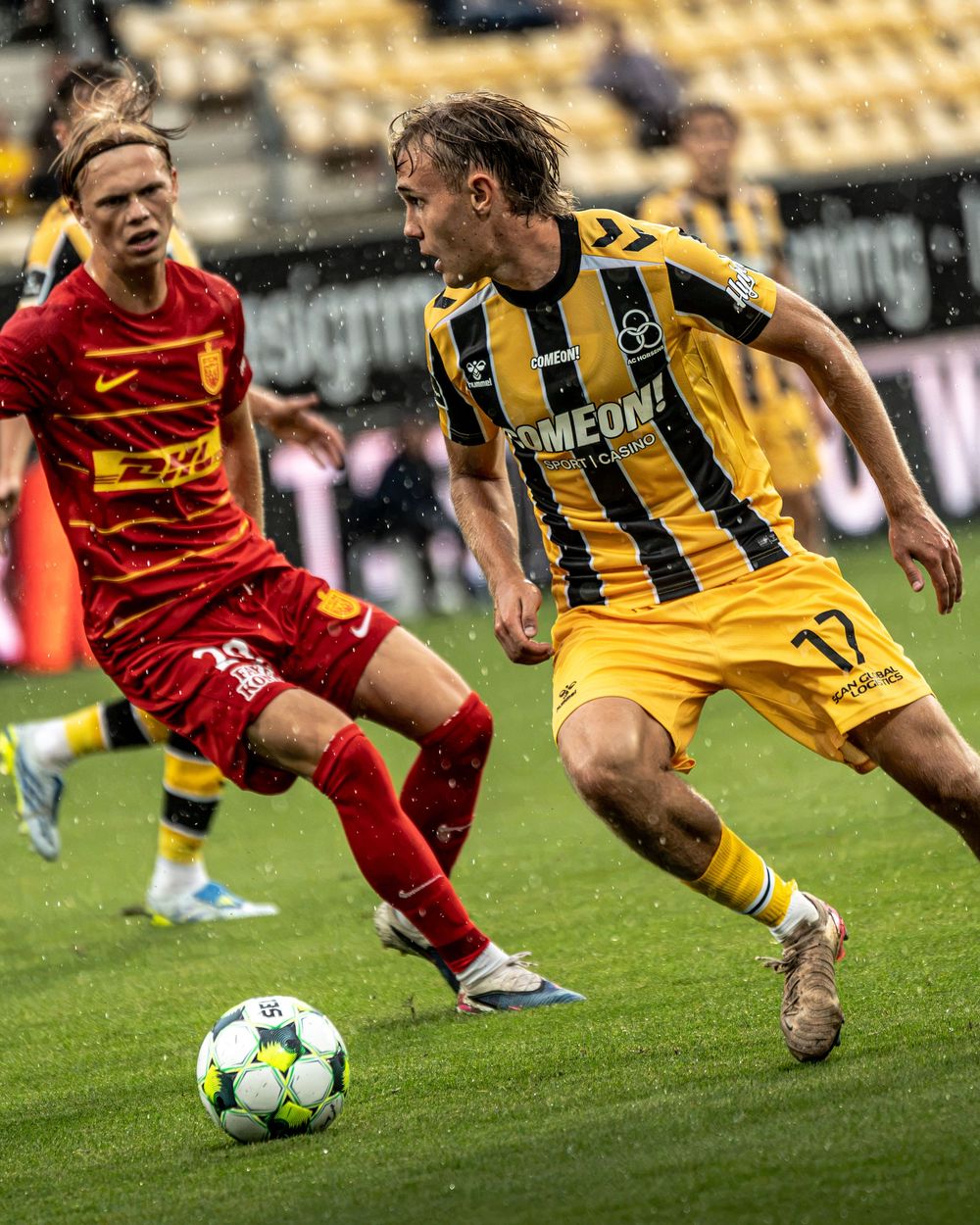 A yellow-clad footballer dribbles past a red-shirted opponent during a Danish football league match.