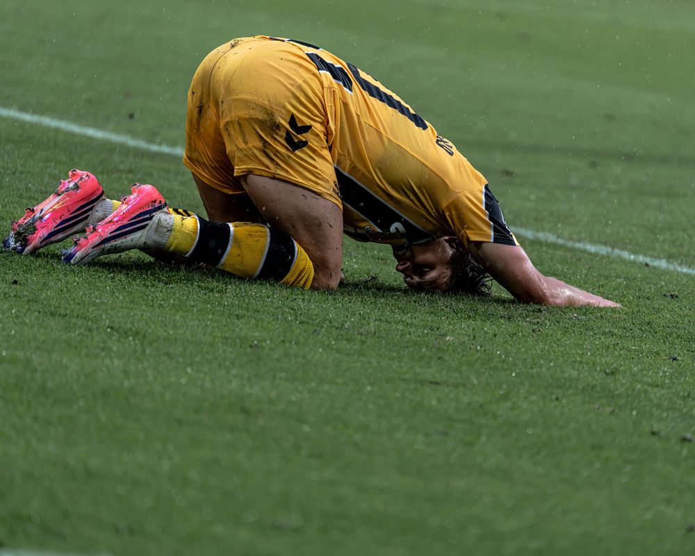 Soccer player in yellow jersey falls to the ground on the grass during a football match.
