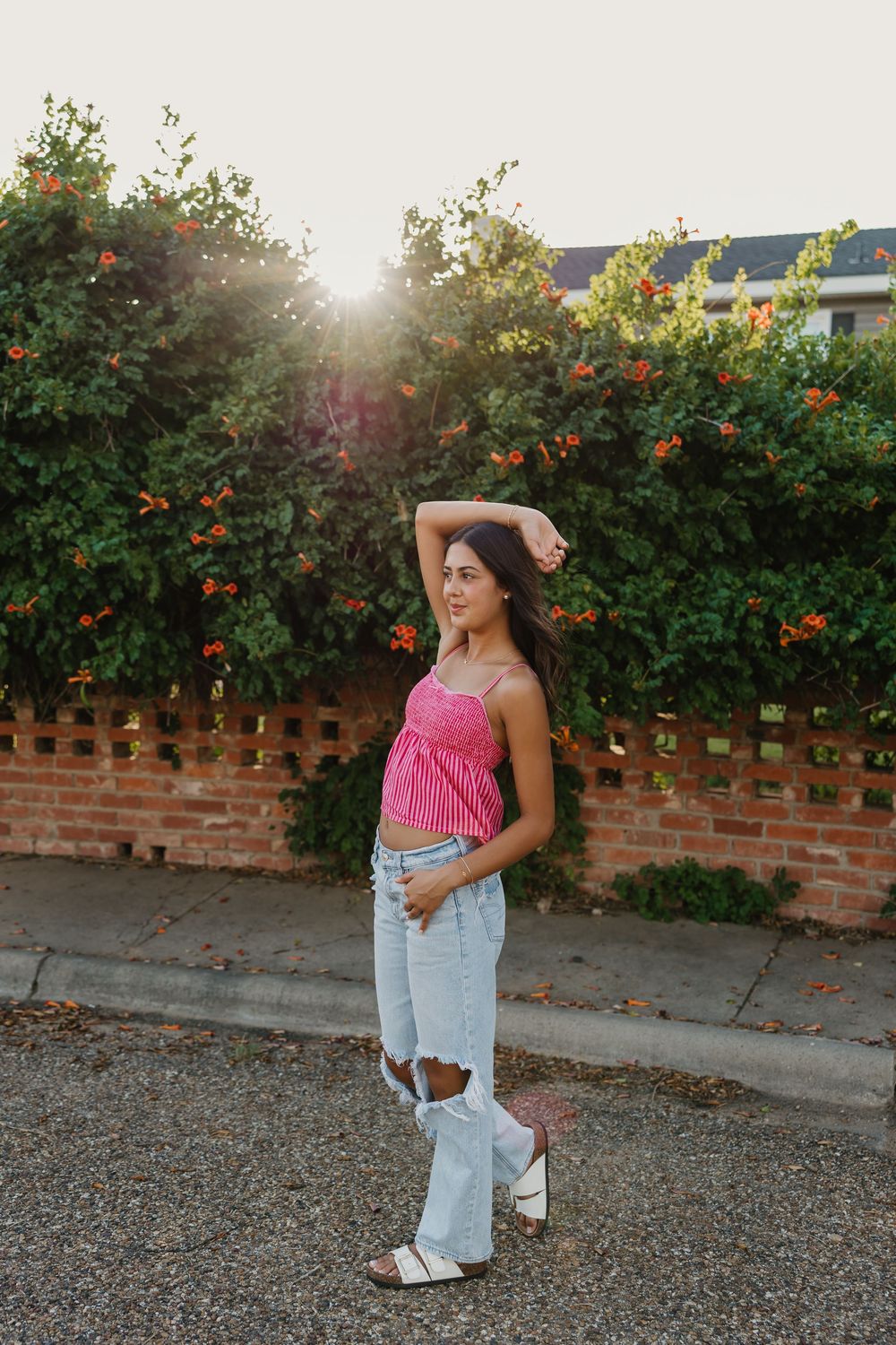 Senior girl wearing fun outfit and taking portraits in front of brick wall covered in flowers and greenery in Tulia, Texas
