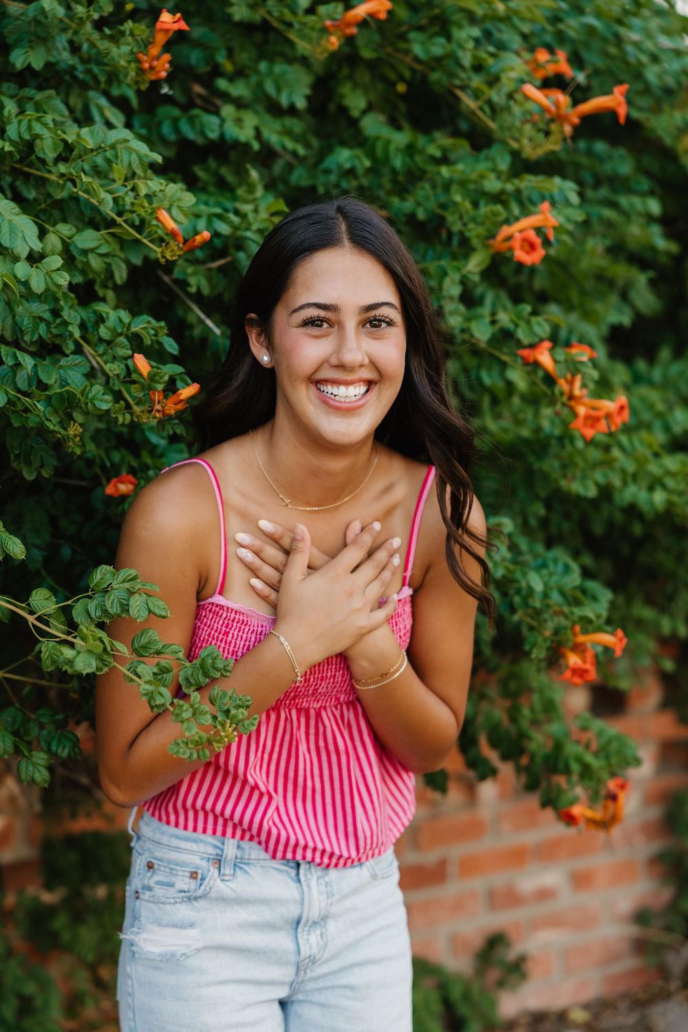 A girl laughing during senior portraits in Tulia Texas backed into flowers and greenery.