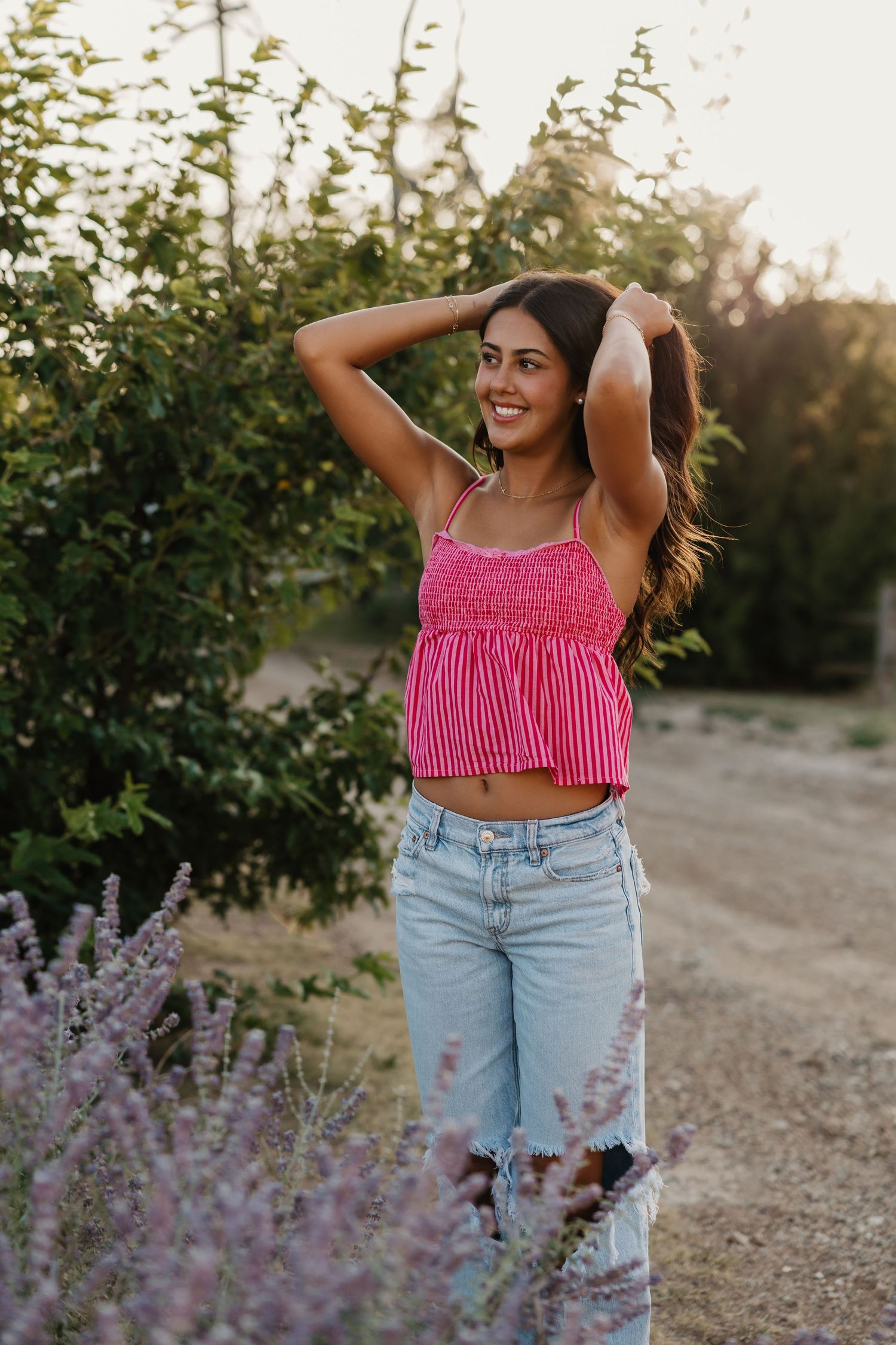 A girl standing in front of purple flowers and greenery posing for senior portraits in Tulia Texas