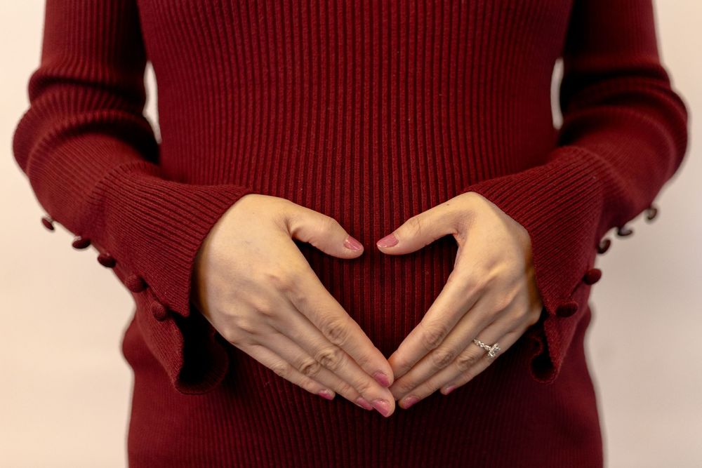 Pregnant woman in red sweater forming heart shape with hands over baby bump.