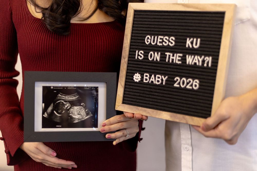 Couple holding ultrasound photo and letter board announcing Baby 2026 pregnancy reveal.