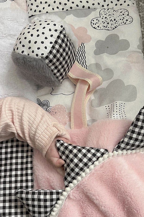 Pink and black gingham baby blanket set with polka dot hat and cloud print fabric on a soft play mat.