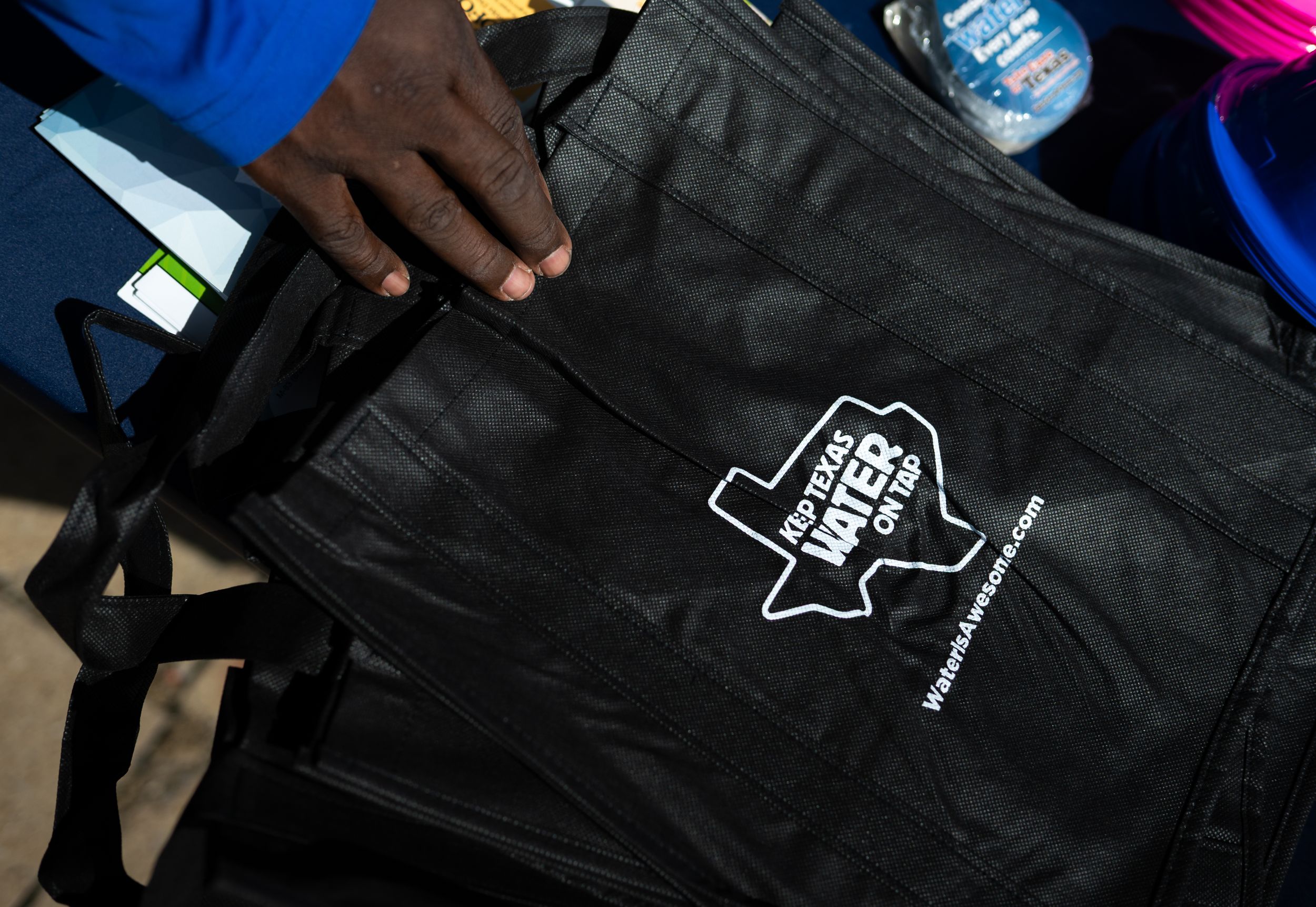 Black reusable tote bag with Texas Votes On logo held by person at voter registration event.