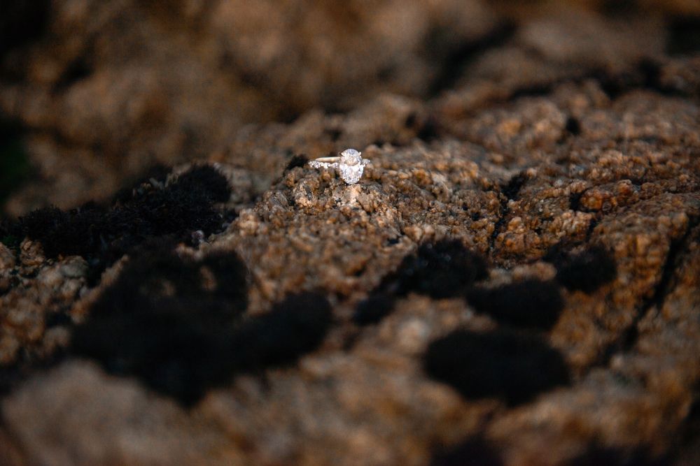 Diamond engagement ring resting on rugged brown rock surface, showcasing elegant solitaire setting in natural outdoor setting.