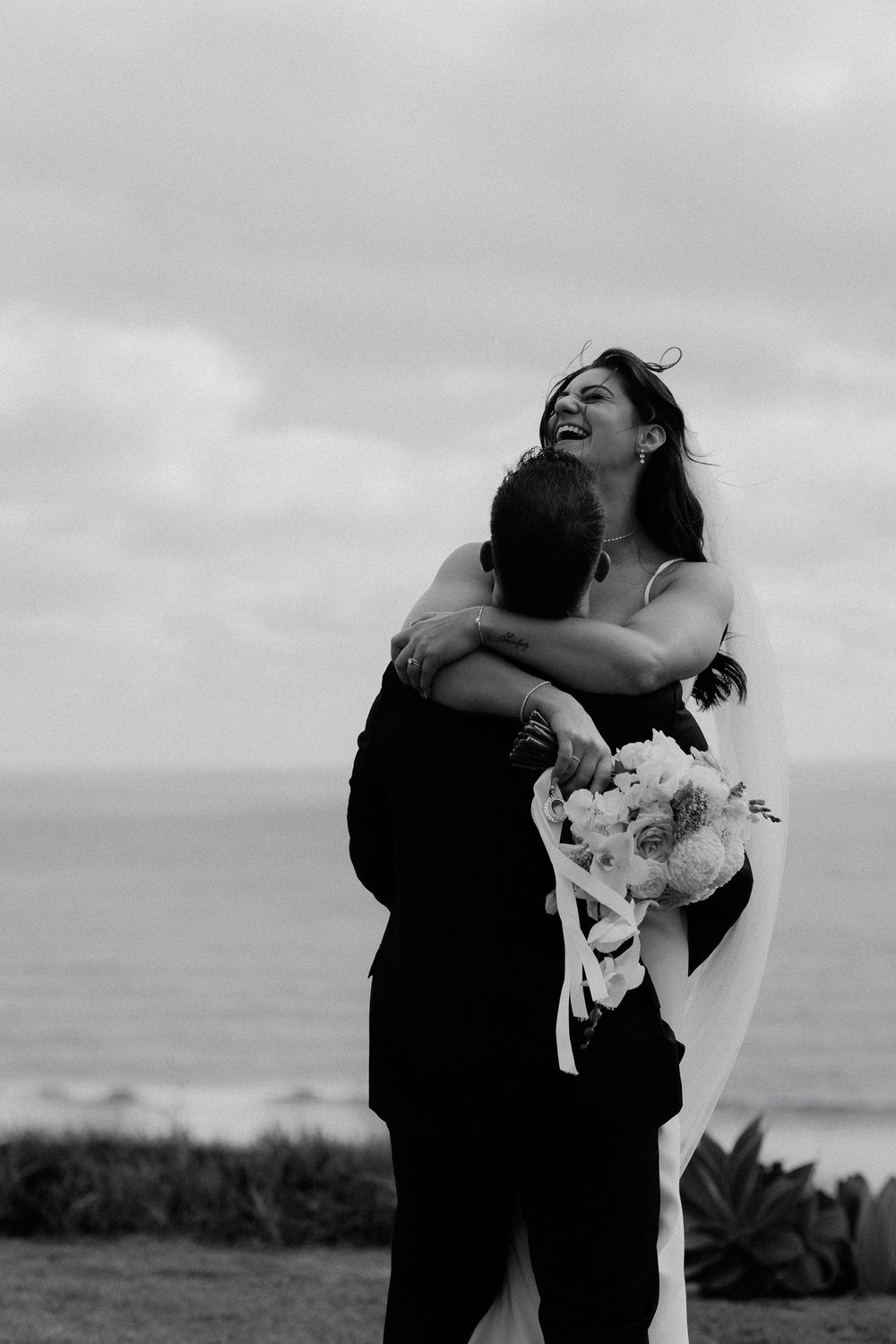 A romantic black and white photo series shows a couple embracing and dancing together on a cloudy day outdoors.