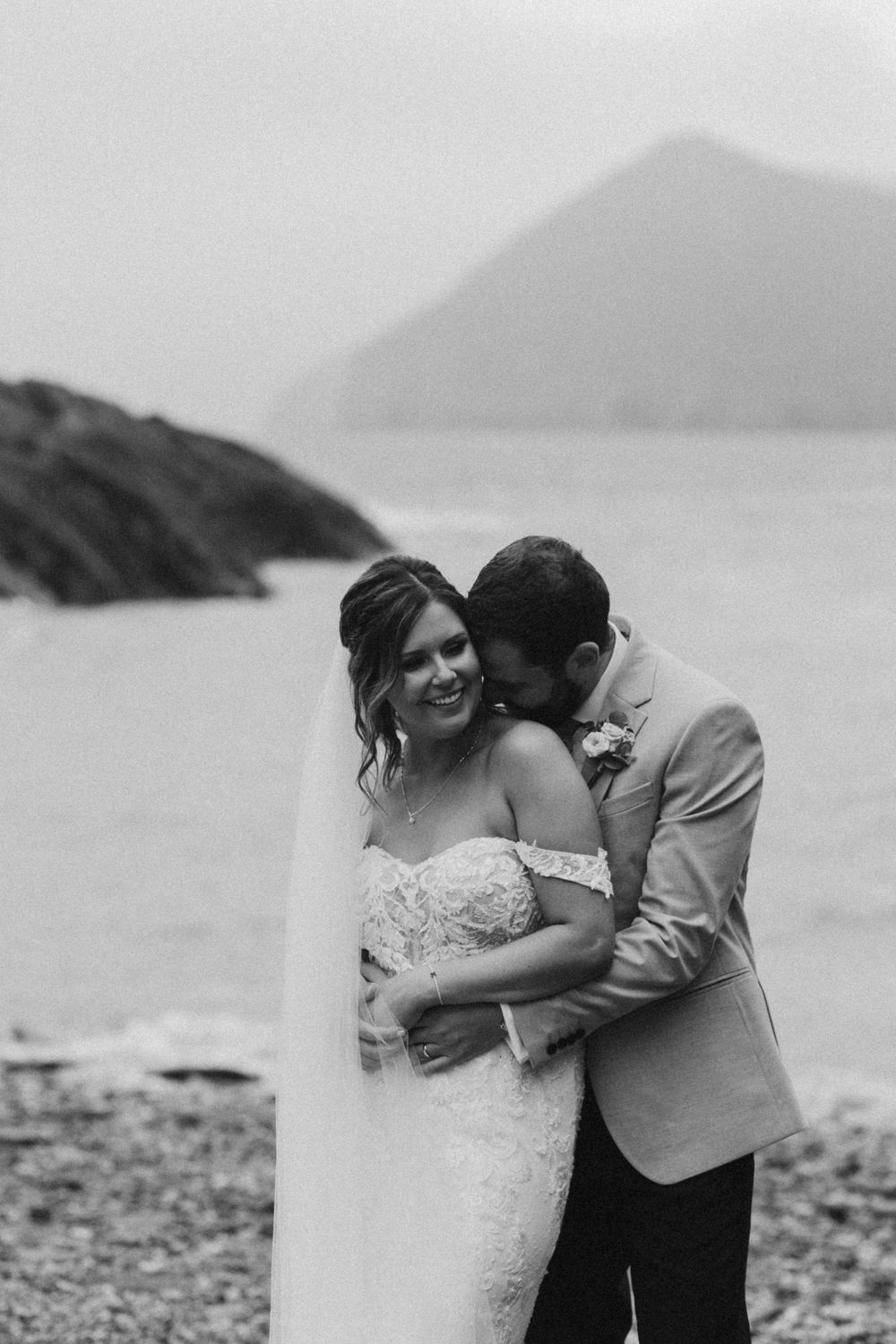 Black and white portrait of bride and groom sharing intimate moment by seaside.
