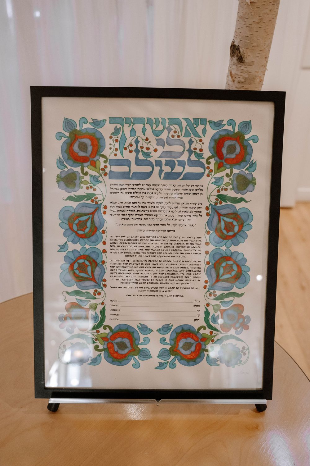 Framed colorful Jewish ketubah marriage contract with Hebrew text and floral folk art design displayed at wedding.