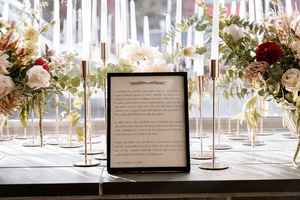 Elegant wedding table display with framed vows, white candles, and floral arrangements featuring red and white blooms.