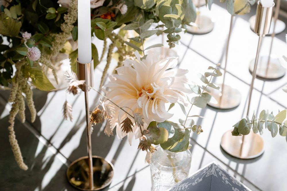 Elegant wedding table centerpiece with white dahlia, eucalyptus greenery, and gold candle holders casting soft shadows.