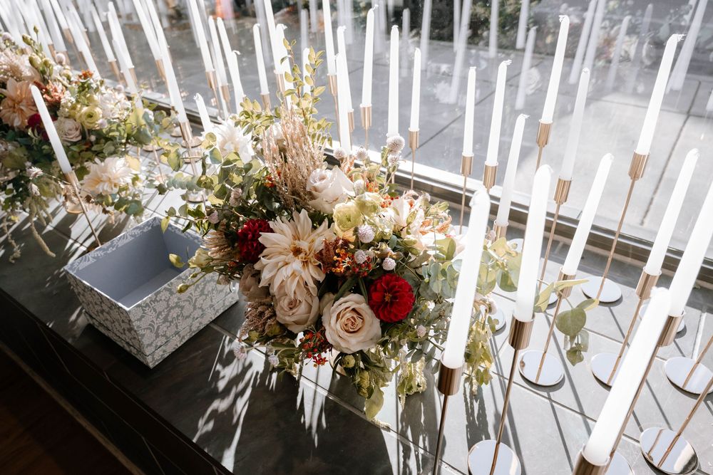 Elegant wedding centerpiece with blush, red, and cream flowers surrounded by tall white taper candles on a dark table.