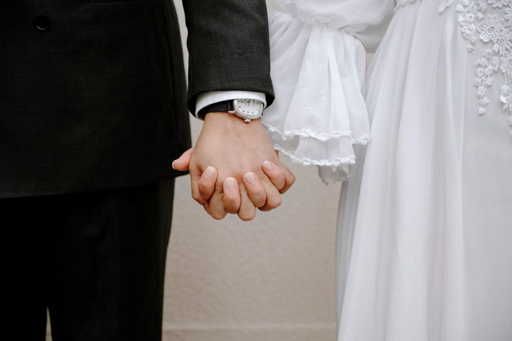 Bride and groom holding hands at wedding ceremony, woman in white dress and man in black suit.