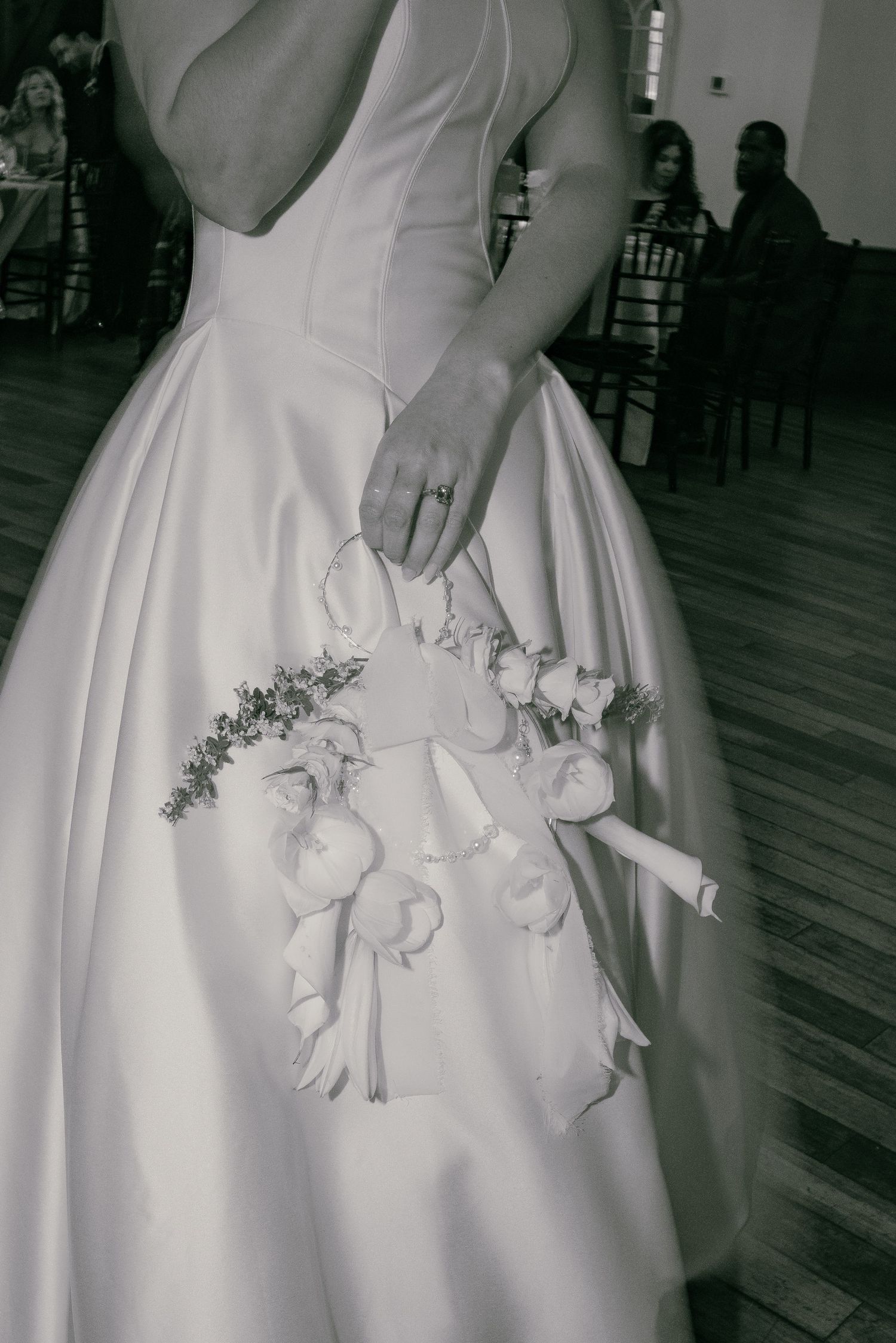 Black and white photo of bride in satin ball gown holding a small floral bouquet at the reception.
