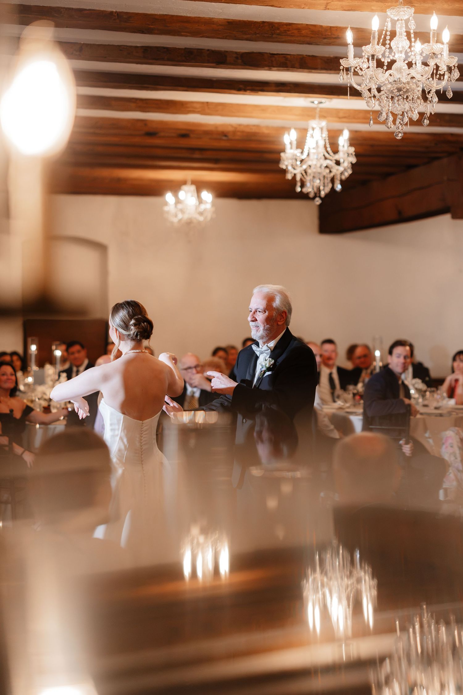 Bride shares a father-daughter dance under crystal chandeliers at elegant wedding reception.