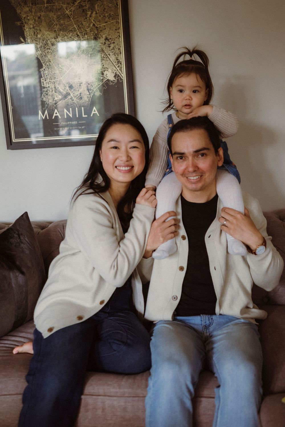 Happy family of three posing on a couch with a Manila map poster in the background.