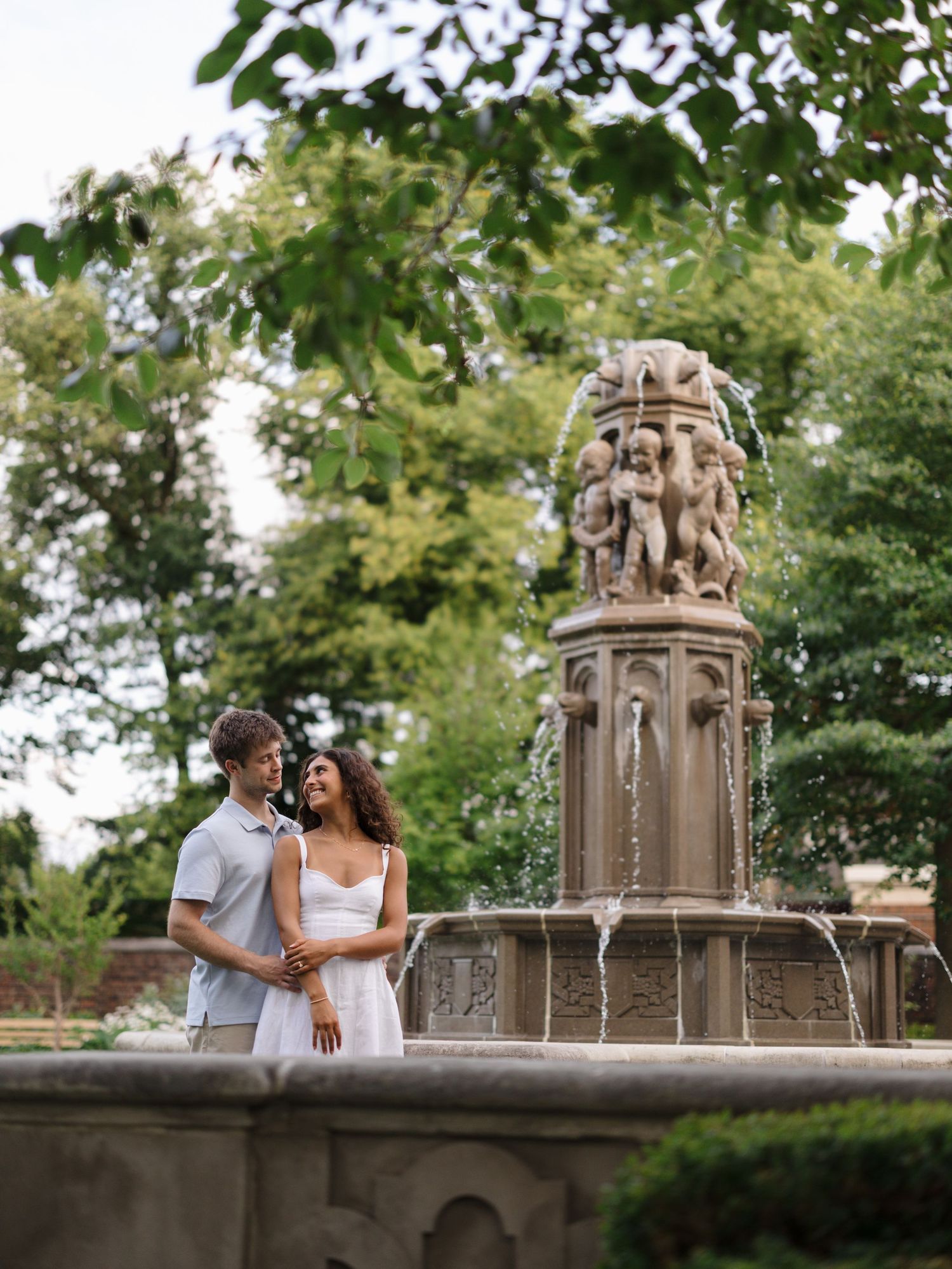 Romantic couple embracing near an ornate stone fountain in a beautiful outdoor garden park.