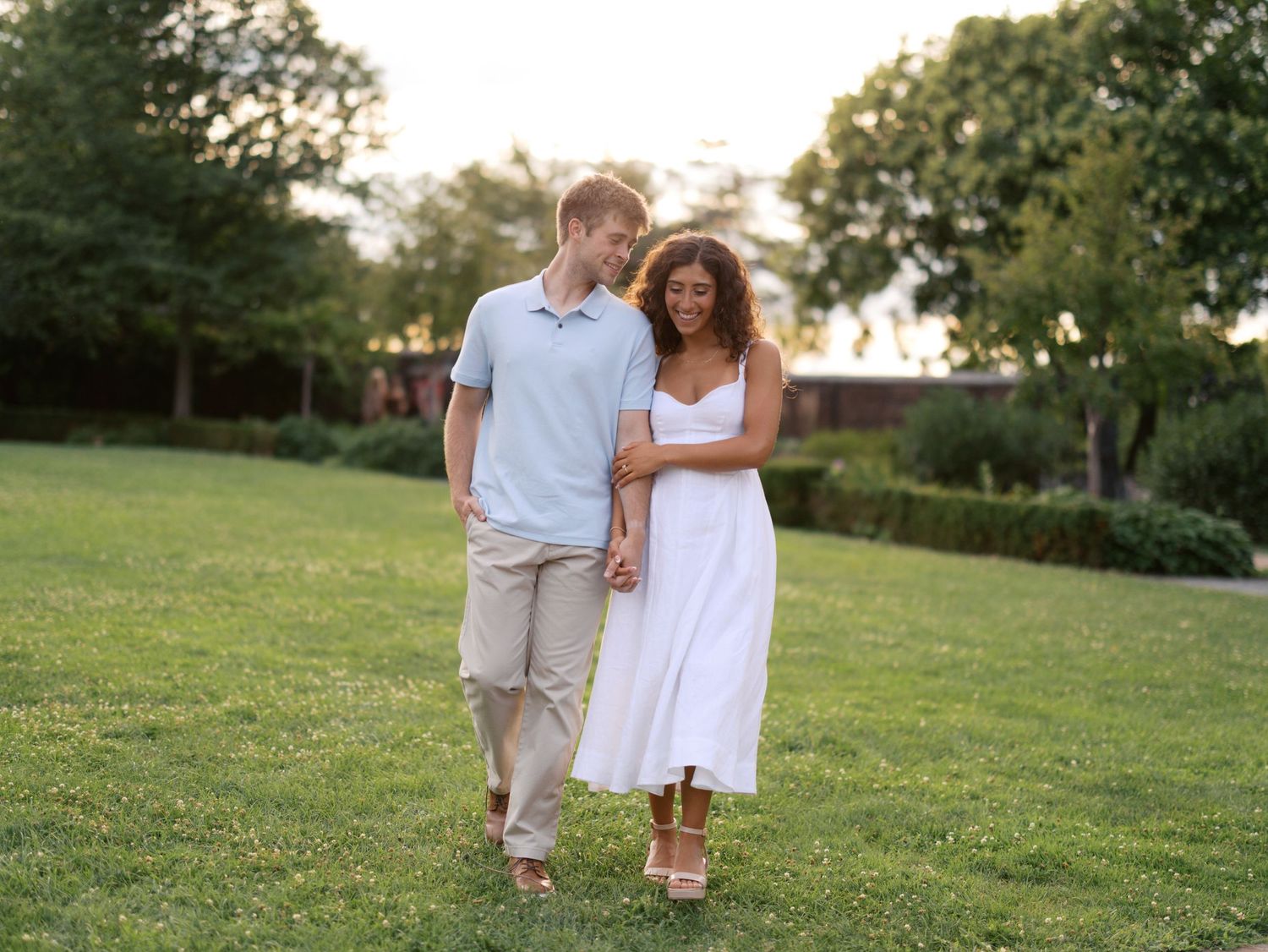 Happy couple walking hand in hand across a sunny green lawn at golden hour.