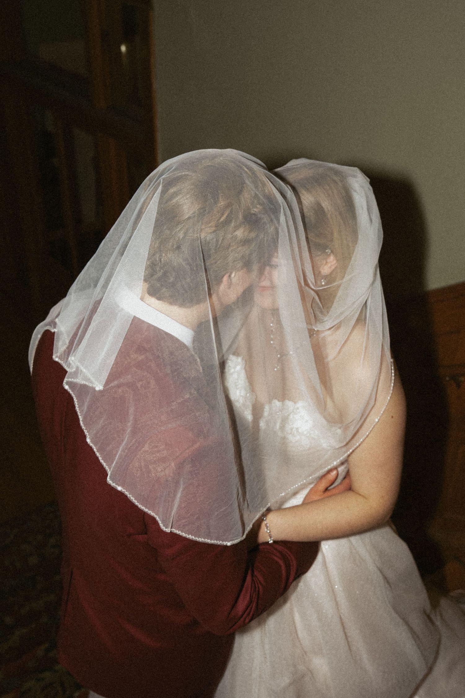 Bride and groom sharing a romantic kiss under a white wedding veil during their ceremony.