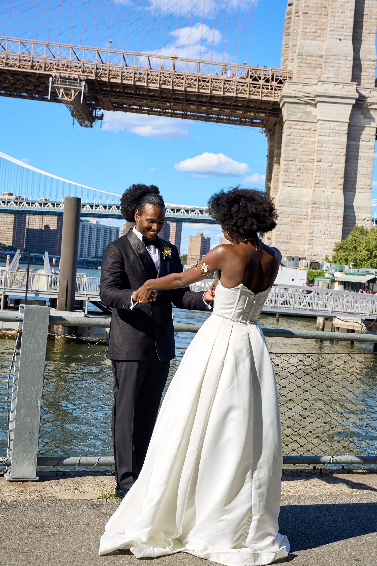 A bride and groom share a joyful moment by the Brooklyn Bridge waterfront on their wedding day.