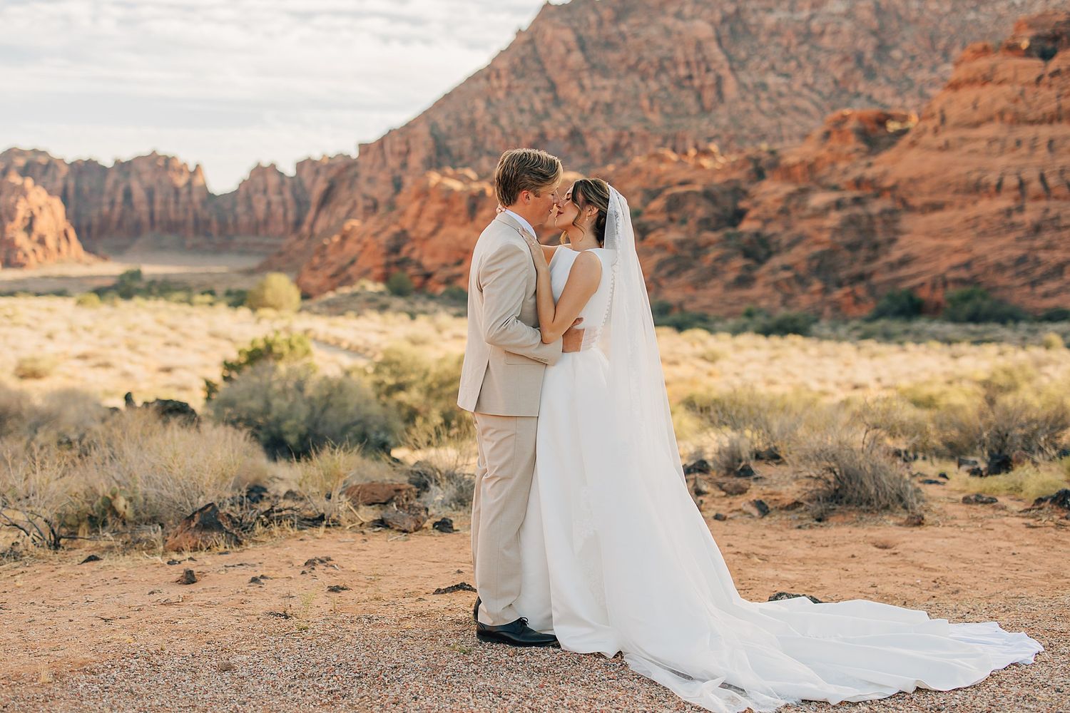Bride and groom share a romantic kiss at Snow Canyon State Park with stunning red rock formations backdrop.