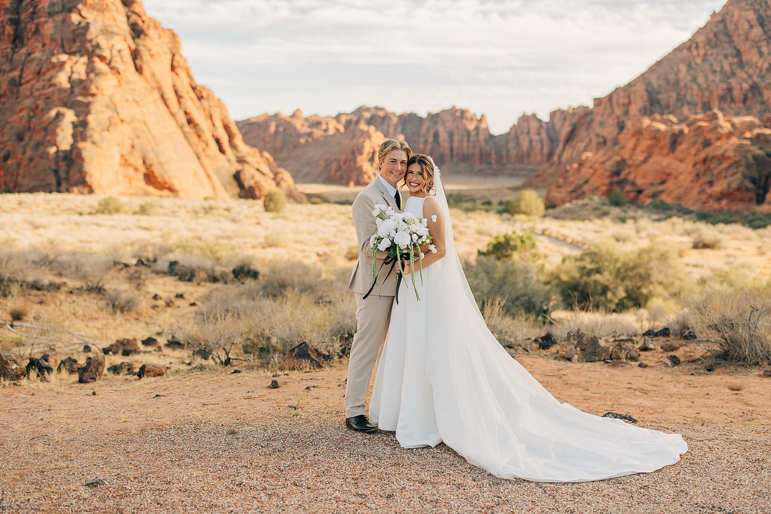 Bride and groom pose together in front of stunning red rock canyon landscape during outdoor desert wedding ceremony.