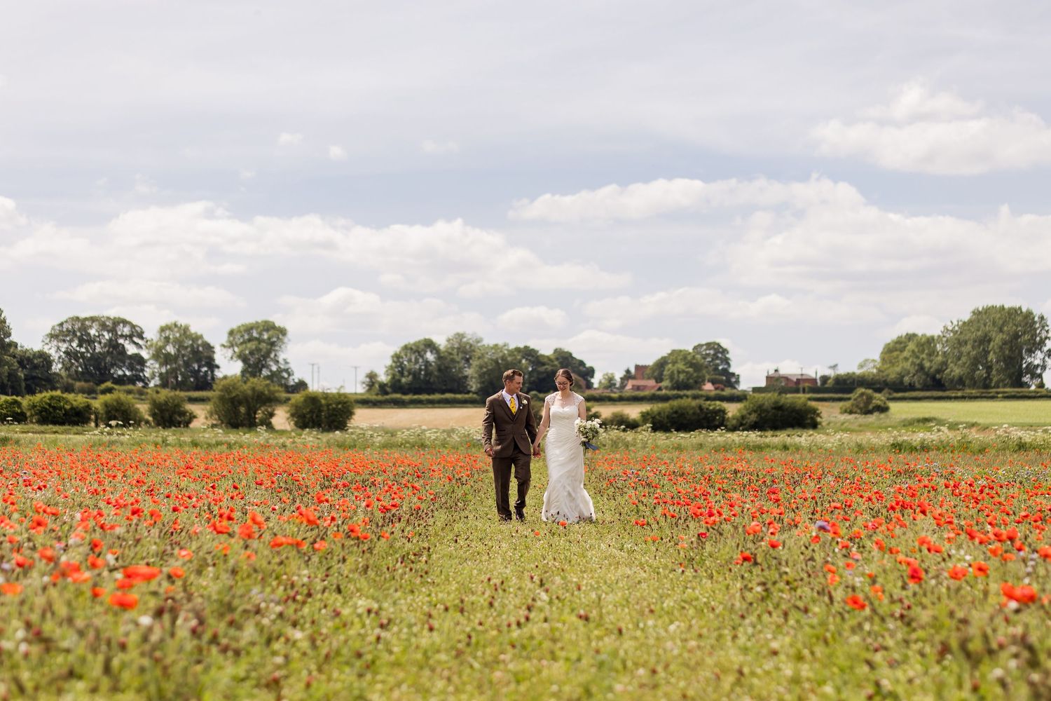 Bride and groom share a romantic kiss on a wooden bridge surrounded by lush green trees in a garden setting.