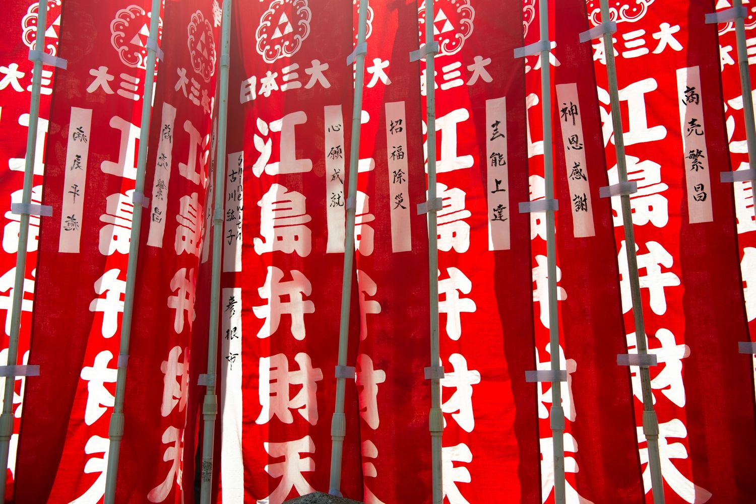 Red Japanese festival banners with gold kanji characters displayed at Enoshima shrine, Japan.