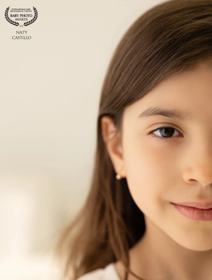Close-up portrait of a young girl with brown hair and blue eyes, subtle smile, fine art baby photography.