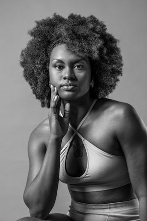 Black and white portrait of a woman with natural afro hair wearing a crop top, posing with hand on chin.