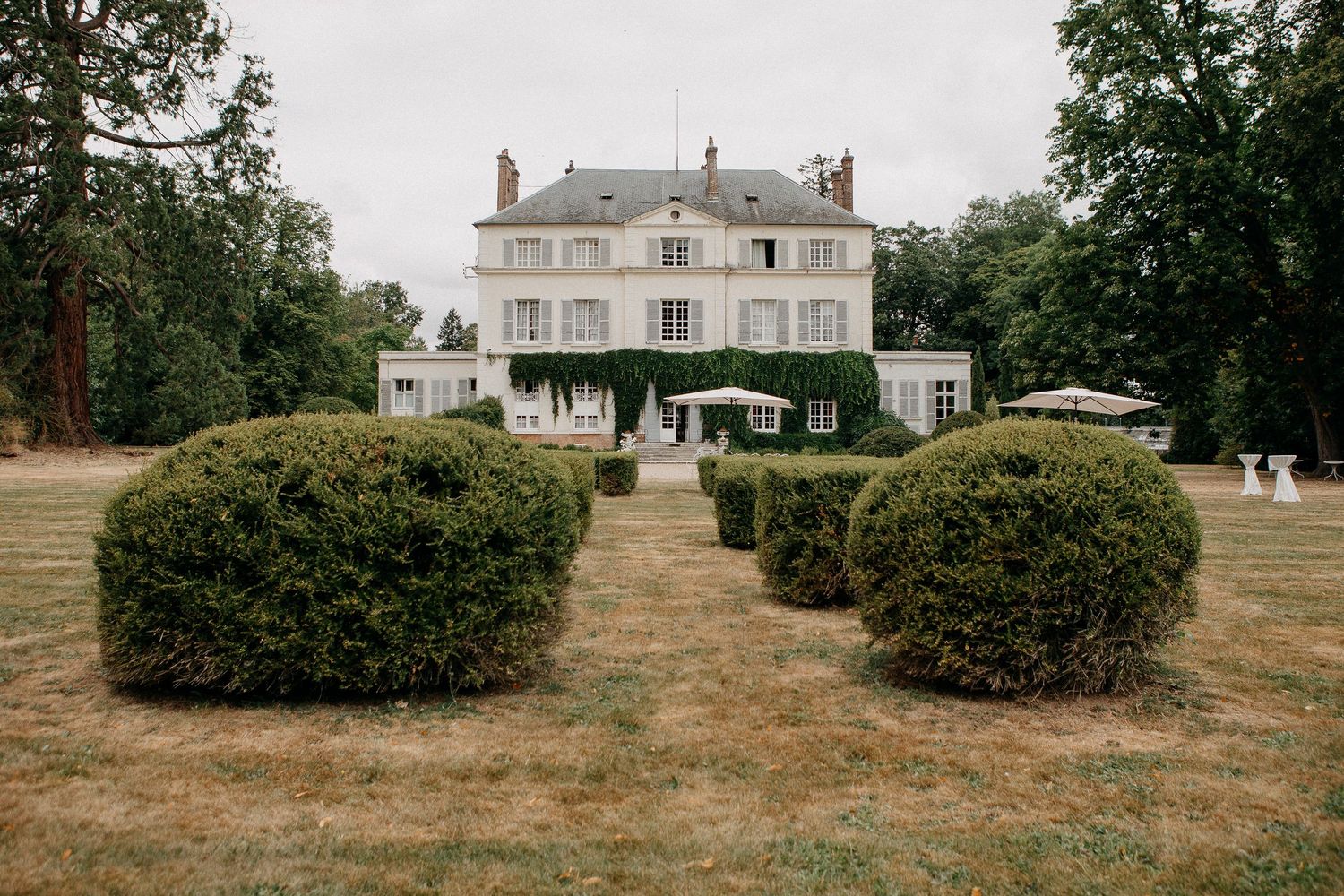 Elegant French château surrounded by manicured hedges and lush green trees on a sprawling estate lawn.