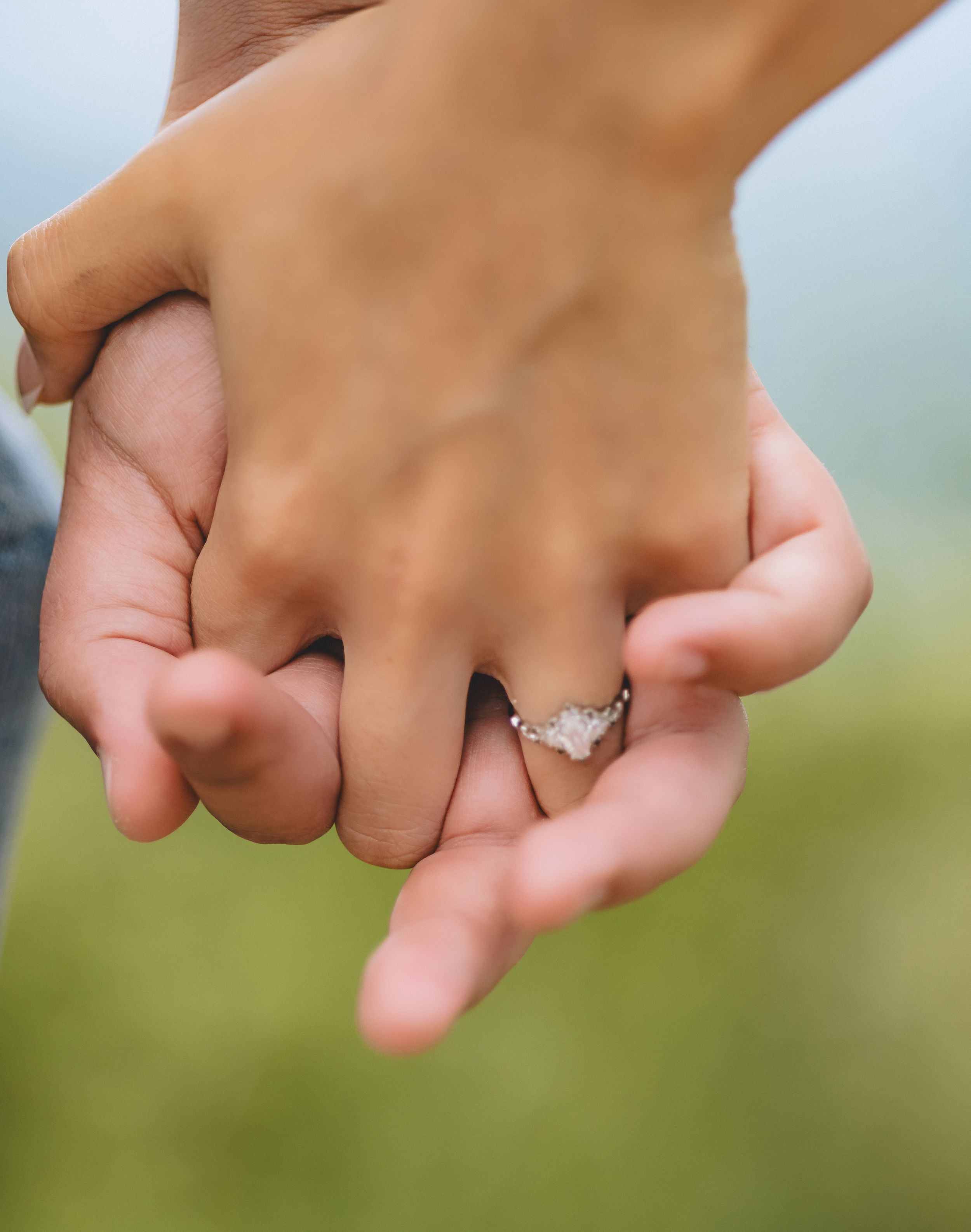 Two hands with engagement rings join together in a symbolic gesture against a soft blurred green background.