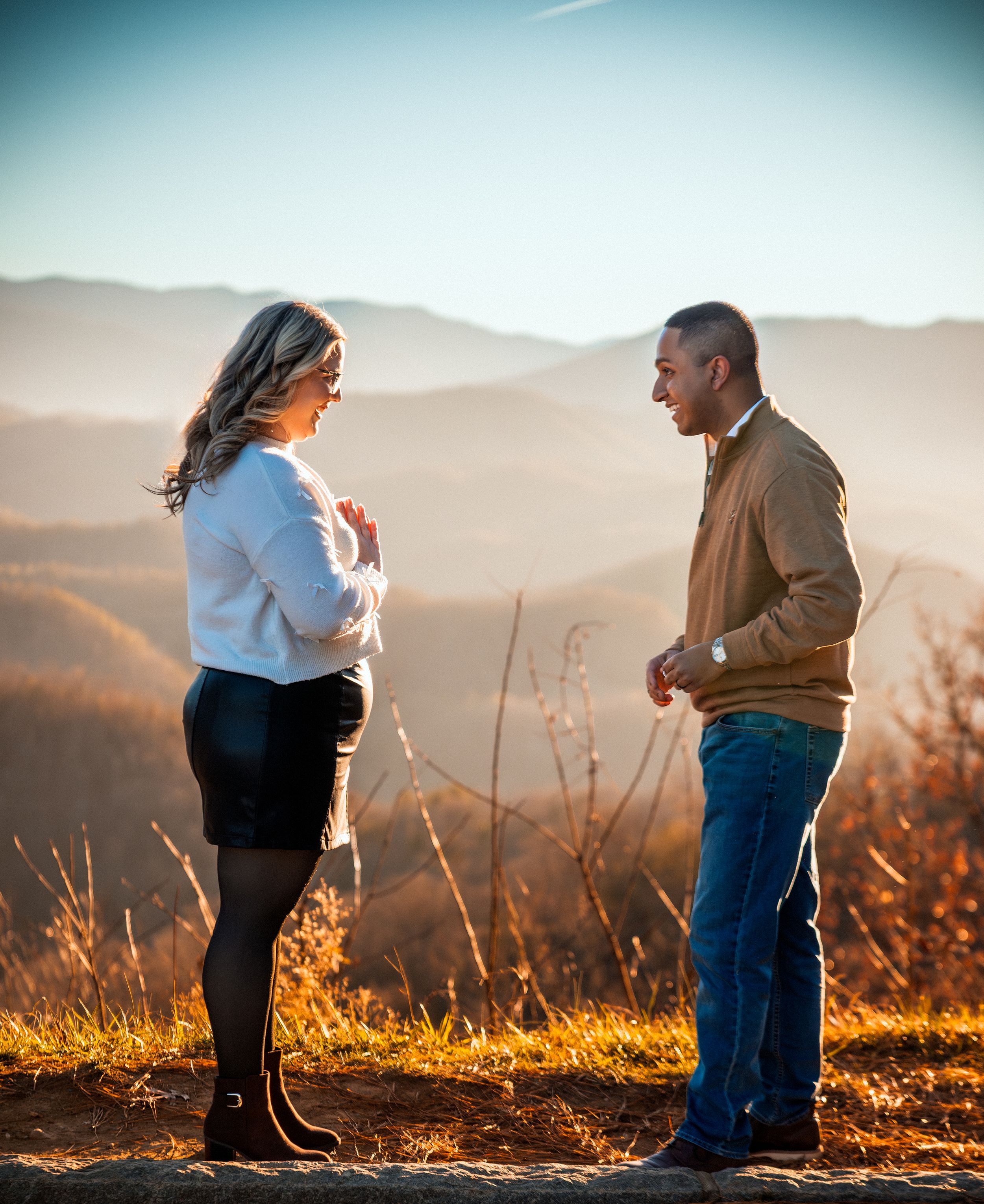 A couple stands silhouetted against a golden sunset in the mountains during an engagement photo session.