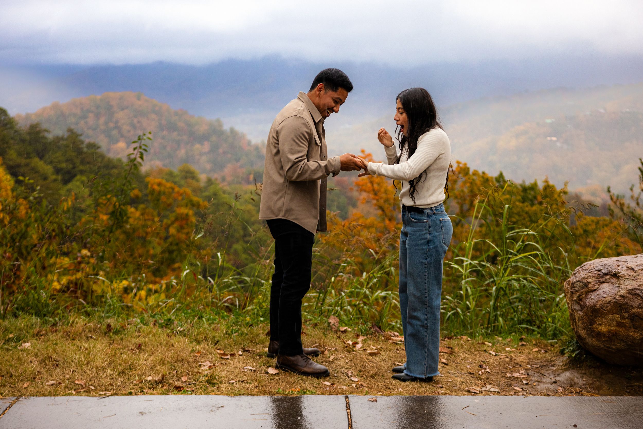 A couple shares a romantic moment in a field of wildflowers with mountains in the background at sunset.