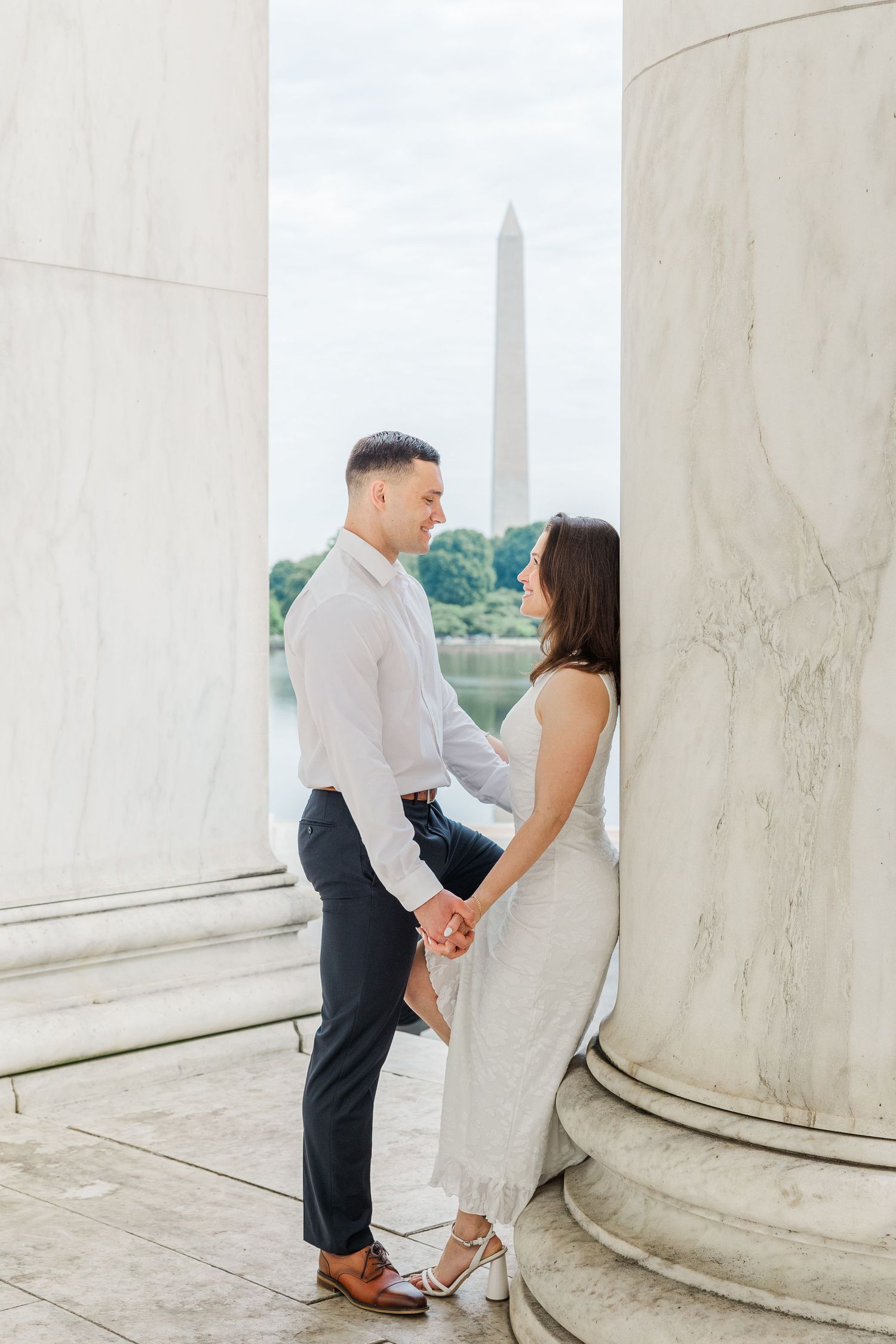 Couple holding hands between marble columns at the Jefferson Memorial with Washington Monument reflected in the Tidal Basin.