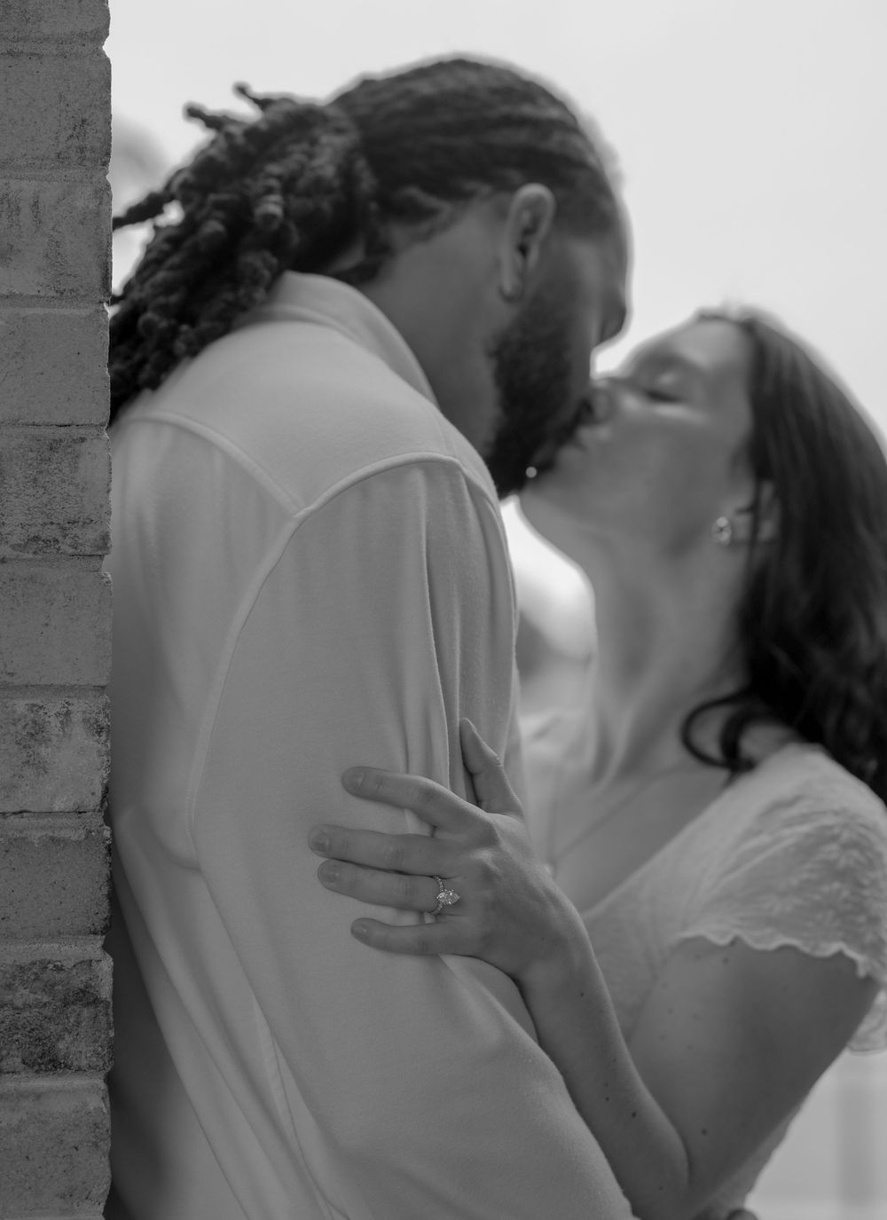 Black and white photo of a couple sharing a romantic kiss, bride wearing wedding dress with engagement ring visible.