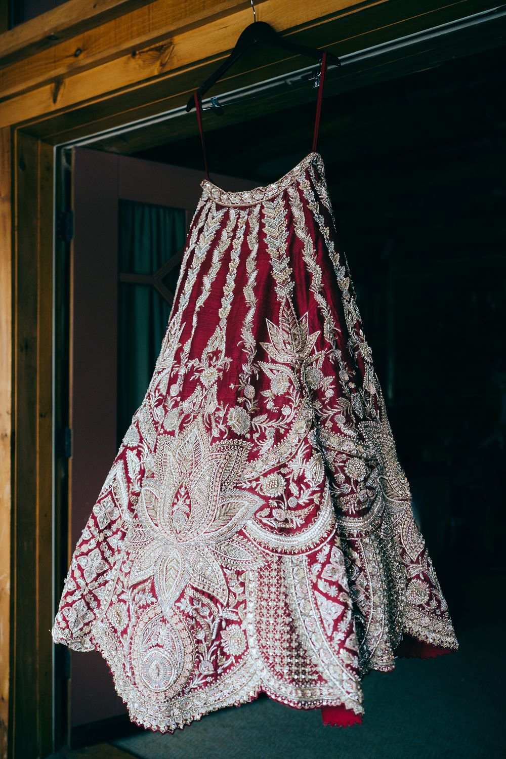 Ornate red and silver embroidered bridal lehenga skirt hanging on display, featuring intricate floral beadwork patterns.