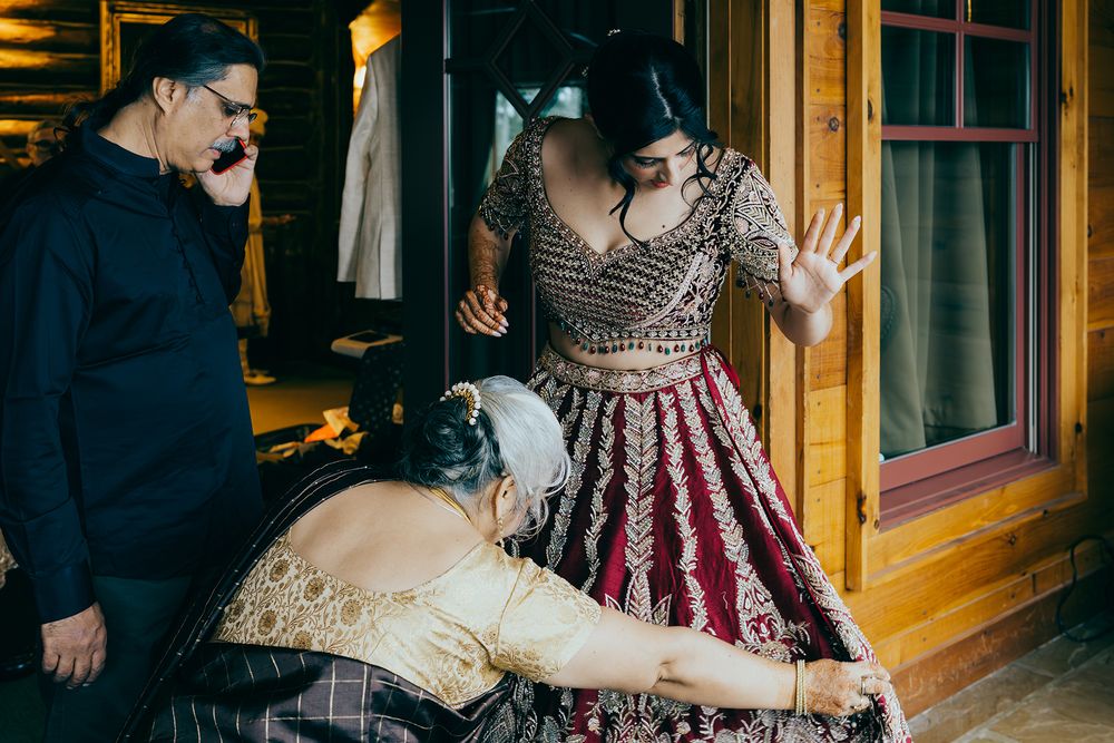 Women in traditional Indian attire being assisted with a bridal lehenga fitting inside a rustic wooden venue.