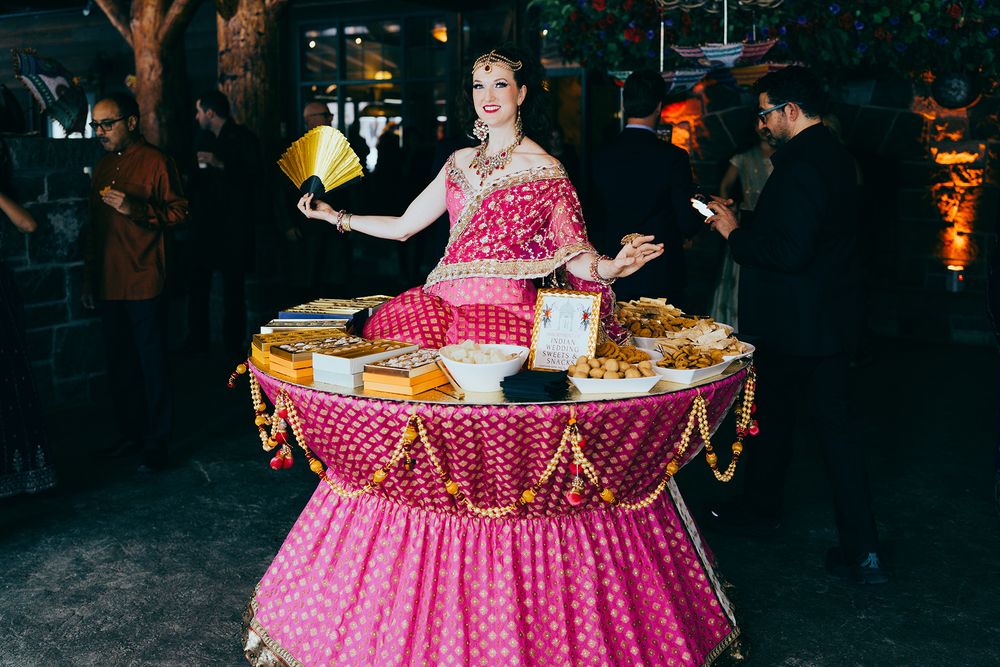 Woman in pink saree serving food at a decorated buffet table at an Indian cultural event.
